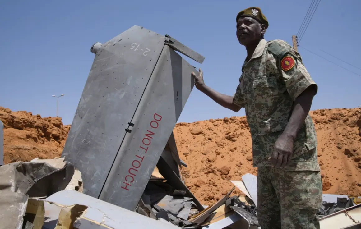 Seorang pria berdiri di lubang yang dipenuhi komponen pesawat tak berawak pada 29 Maret 2026, di El-Obeid, Sudan.