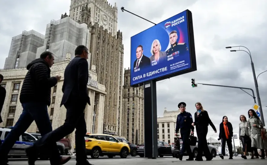 Para pejalan kaki berjalan melewati gedung Kementerian Luar Negeri Rusia dan sebuah poster kampanye untuk pemilihan Duma Negara Rusia di Moskow, pada tanggal 7 September.