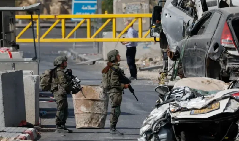 Tentara Zionis Israel di tengah reruntuhan mobil dan bangunan rakyat Palestina.